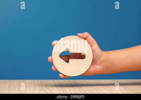 Pfeil zeigt auf blauem Hintergrund nach links. Banner mit einem Pfeil in einem hölzernen Kreis in einer Hand Nahaufnahme zeigt nach links mit Kopierraum. Stockfoto