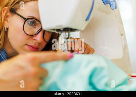 Die Schneiderin in der Brille arbeitet an der Nähmaschine an ihrem Arbeitsplatz in der Werkstatt Stockfoto