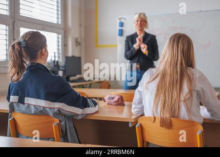 Rückansicht von zwei Schülerinnen während einer Vorlesung im Klassenzimmer mit Blick auf Lehrerinnen, die an einer Tafel unterrichten und schreiben Stockfoto