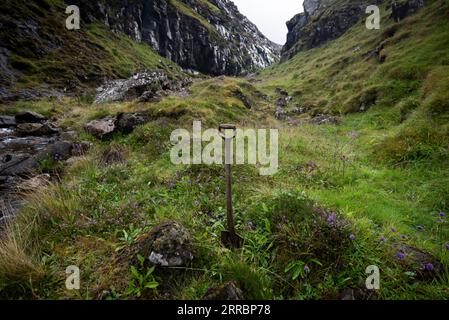 Eine alte Schaufel bleibt in der Nähe einer Felsschlucht vergessen, die Wasser für eine nahe gelegene Farm auf den Färöern liefert. Stockfoto