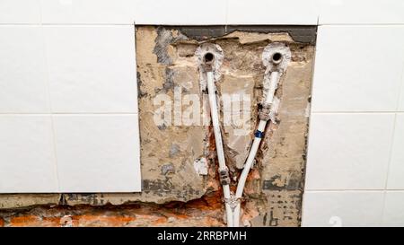 Alte Wasserversorgung für den Wasserhahn im Badezimmer und Rohrleitungen mit Metall-Kunststoff-Rohren in gemeißelten Wänden unter entfernten Keramikfliesen Stockfoto