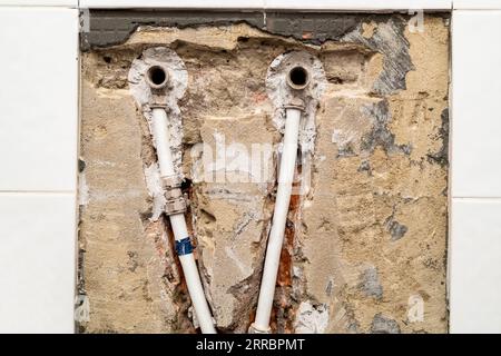 Alte Rohrleitungen mit Metall-Kunststoff-Rohren in gemeißelter Ziegelwand unter entfernten Keramikfliesen Stockfoto