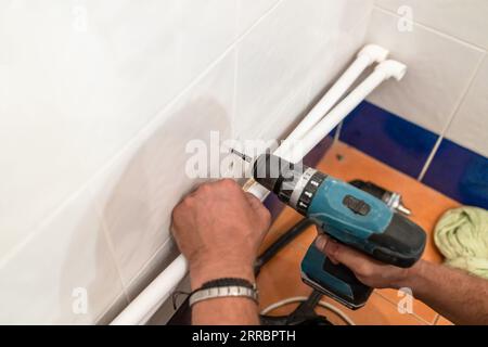 Klempner bohren Loch zum Befestigen neuer Kunststoffrohre mit Bohrer im Badezimmer während der Installation einer neuen Wasserversorgung Stockfoto