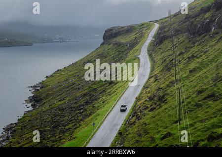 Nachmittagslicht fällt auf einem einsamen Autobahnabschnitt auf Streymoy Island mit Eysturoy Island im Hintergrund auf den Färöern. Stockfoto