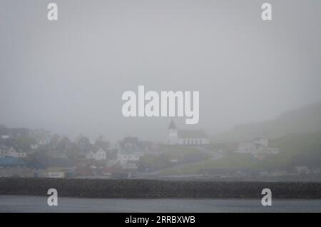 Die Kirche in Ei∂i auf den Färöern, tief im Nebel, von der anderen Seite des Fjords aus gesehen. Stockfoto