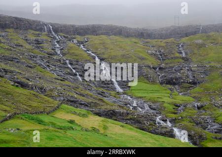 Das Wasser fällt einen Hang über dem Dorf Tjørnuvik auf den Färöern hinab. Stockfoto