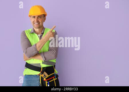 Ein reifer Baumeister, der auf etwas auf Fliederhintergrund zeigt Stockfoto