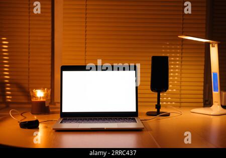 Moderner Arbeitsplatz des Freiberuflers am Abend. Laptop mit leerem Bildschirm isoliert. Nachtarbeitskonzept. Stockfoto