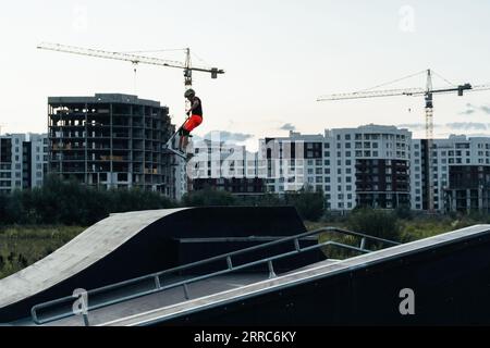 Aktive Freizeitgestaltung für Kinder auf einem Roller. Ein Junge auf einem Roller in einem Skatepark führt Sprünge und Tricks durch. Extremes Springen auf einem Roller. Stockfoto