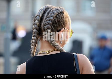 Mädchen mit geflochtenen Zöpfen, die auf einer Straße spazieren. Weibliche Frisur und Mode in der Stadt Stockfoto