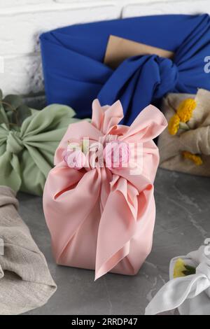 Furoshiki-Technik. Viele Geschenke in Stoff auf einem grauen Tisch Stockfoto