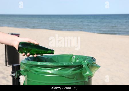 Frau, die Glasflasche in den Mülleimer am Strand wirft, Nahaufnahme. Recyclingkonzept Stockfoto