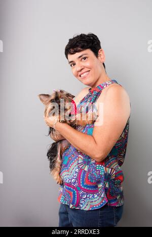 Eine Frau hält liebevoll einen schönen Yorkshire-Terrier. Isoliert auf grauem Hintergrund. Stockfoto