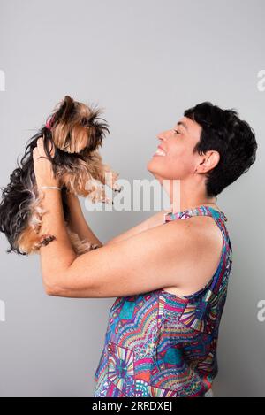 Eine Frau hält liebevoll einen schönen Yorkshire-Terrier. Isoliert auf grauem Hintergrund. Stockfoto