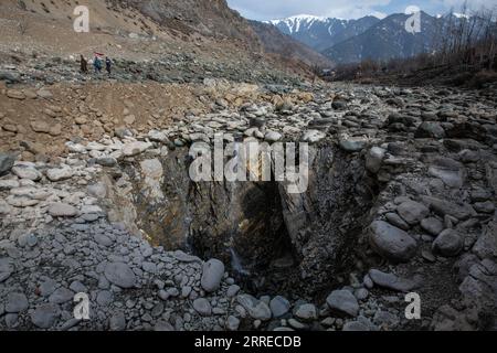 220218 -- SRINAGAR, 18. Februar 2022 -- Menschen laufen in der Nähe eines senkrechten Senklochs, das sich in der Mitte eines Flussbettes in einem Dorf im Bezirk Anantnag entwickelt hat, etwa 94 km südlich von Srinagar, der Sommerhauptstadt des von Indien kontrollierten Kaschmirs, 18. Februar 2022. Ein vertikales Senken, das sich in der Mitte eines Flussbettes entwickelt hat, hat einen Süßwasserstrom im von Indien kontrollierten Kaschmir gefressen, sagten Beamte am Donnerstag. Das Senkenloch hat den gesamten Lauf des Bachwassers in es abgeführt und den flussabwärts gelegenen Teil trocken gelassen, wodurch Forellenfische in großer Zahl getötet wurden. Sie hat auch unermessliche Schäden verursacht Stockfoto