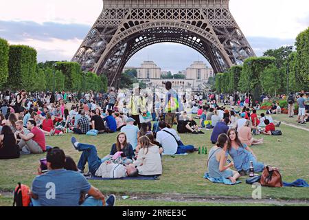 Paris, Souvenirverkäufer, die auf den Champs de Mars arbeiten, verkaufen Bier und Wein an Touristen, die am Abend ein Picknick machen und auf die Lichtshow im Eiffelturm warten Stockfoto