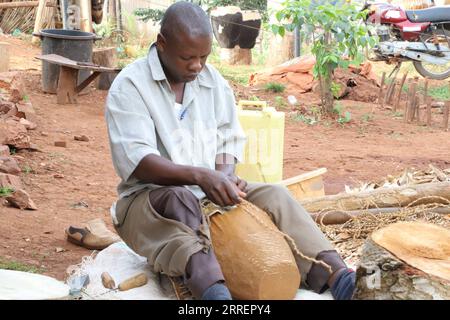 220312 -- MPIGI, 12. März 2022 -- Francis Yiga, ein Handwerker, arbeitet an einer Trommel im Dorf Mpambire im Bezirk Mpigi, Uganda, 10. März 2022. Mpambire, ein Dorf im zentralen ugandischen Bezirk von Mpigi, ist als Geburtsort für Trommeln im Land bekannt. Das Dorf ist mit provisorischen Werkstätten gespickt, in denen die Trommeln aus Baumstämmen und Tierhäuten und Fellen hergestellt werden. ZUM Feature: Jahrhundertealte Tradition des Trommelbaus in Uganda gegen die Moderne UGANDA-MPIGI-TROMMELBAUER ZhangxGaiping PUBLICATIONxNOTxINxCHN Stockfoto