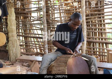 220312 -- MPIGI, 12. März 2022 -- Ein Schlagzeuger arbeitet an einer Trommel im Dorf Mpambire im Bezirk Mpigi, Uganda, 10. März 2022. Mpambire, ein Dorf im zentralen ugandischen Bezirk von Mpigi, ist als Geburtsort für Trommeln im Land bekannt. Das Dorf ist mit provisorischen Werkstätten gespickt, in denen die Trommeln aus Baumstämmen und Tierhäuten und Fellen hergestellt werden. ZUM Feature: Jahrhundertealte Tradition des Trommelbaus in Uganda gegen die Moderne UGANDA-MPIGI-TROMMELBAUER ZhangxGaiping PUBLICATIONxNOTxINxCHN Stockfoto