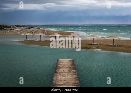 Nin, Kroatien - leerer Queen's Beach in der kleinen mediterranen Stadt Nin am Ende des Sommers mit Schilfsonnenschirmen, kleinem Pier und türkisfarbener Adria Stockfoto