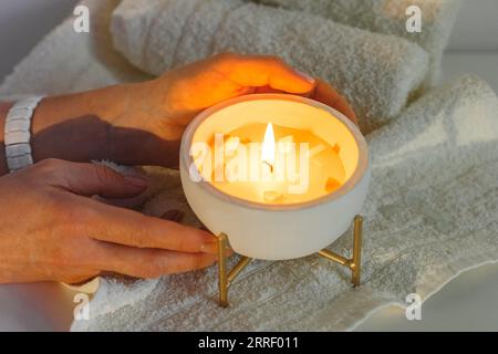 Eine Frau legt eine brennende Duftkerze neben weiße Handtücher auf den Tisch. Vorbereitung auf den Empfang des Kunden im Spa-Salon. Stockfoto