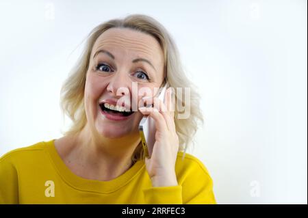 Porträt einer attraktiven, fröhlichen, grauhaarigen Frau, die auf einem Diwan sitzt und auf dem Handy telefoniert, im Haus, in der Wohnung. Hochwertiges Foto Stockfoto