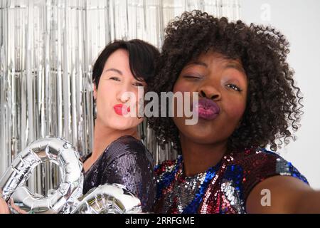 Zwei multirassische Frauen auf einer Party mit einem silbernen Ballon, der ein küssiges Gesicht macht. Zwei Freunde auf einer Party. Stockfoto