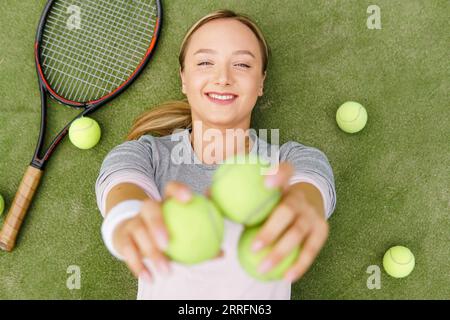 Junge Tennisspielerin, die zwei Tennisbälle in der Hand auf dem Tennisplatz zeigt. Stockfoto