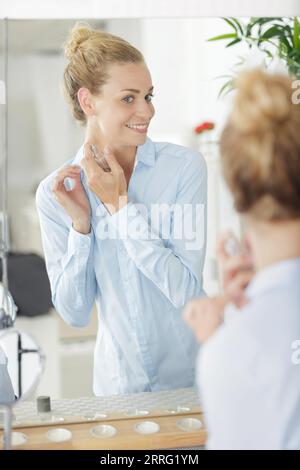 Dame, die in den Spiegel schaut, während sie Parfüm aufträgt Stockfoto