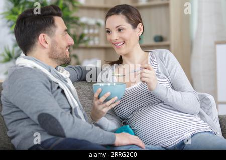 Glückliches Paar sitzt auf dem Sofa und isst Maisflocken Stockfoto