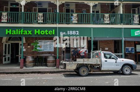 Eine typische australische Szene - Trinker sitzen im Schatten vor einem Pub aus der viktorianischen Zeit und eine 'ute' parkt auf der Straße - Halifax, Queensland, Australien Stockfoto