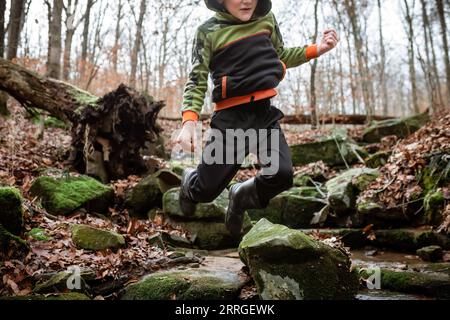 Auf der Herbstwanderung springt das Kind fröhlich über moosbedeckte Felsbrocken Stockfoto