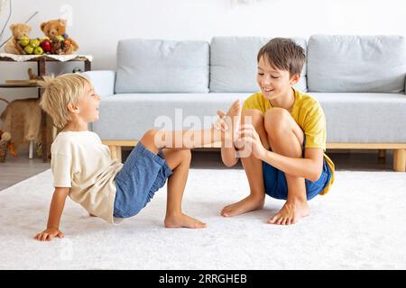 Glückliche positive Kinder, kitzeln auf den Füßen, haben Spaß zusammen, Junge Brüder zu Hause haben einen wunderbaren Tag der Freude zusammen Stockfoto