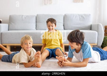 Glückliche positive Kinder, kitzeln auf den Füßen, haben Spaß zusammen, Junge Brüder zu Hause haben einen wunderbaren Tag der Freude zusammen Stockfoto