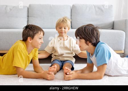 Glückliche positive Kinder, kitzeln auf den Füßen, haben Spaß zusammen, Junge Brüder zu Hause haben einen wunderbaren Tag der Freude zusammen Stockfoto