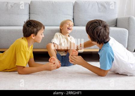 Glückliche positive Kinder, kitzeln auf den Füßen, haben Spaß zusammen, Junge Brüder zu Hause haben einen wunderbaren Tag der Freude zusammen Stockfoto