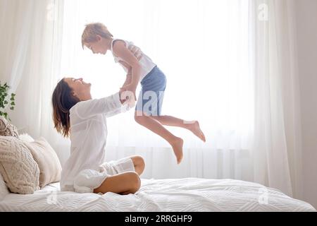 Mutter, die mit ihrem Vorschulkind zu Hause im Bett spielt, Spaß beim Springen und Fliegen hat Stockfoto