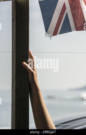 Eine sonnenbeschienene Hand auf einem Fahnenmast mit einem Stück der britischen Flagge, das in der Brise vor einem unscharfen Meereshintergrund in Greve de Lecq Jersey winkt Stockfoto