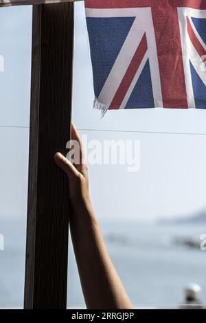 Eine sonnenbeschienene Hand auf einem Fahnenmast mit einem Stück der britischen Flagge, das in der Brise vor einem unscharfen Meereshintergrund in Greve de Lecq Jersey winkt Stockfoto