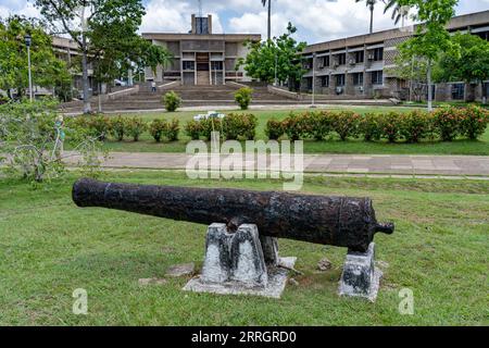 Eine Kanone aus der Kolonialzeit auf dem Independence Plaza in der Hauptstadt Belmopan, Belize. Das Gebäude der Nationalversammlung ist dahinter. Stockfoto