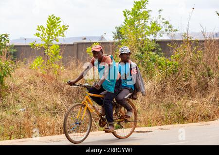 Mandoto, Madagaskar - 1. November 2022: Zwei madagassische Männer fahren mit dem Fahrrad auf einer Landstraße. Zwei madagassische Männer auf einem Fahrrad. Eine führt die andere. Stockfoto