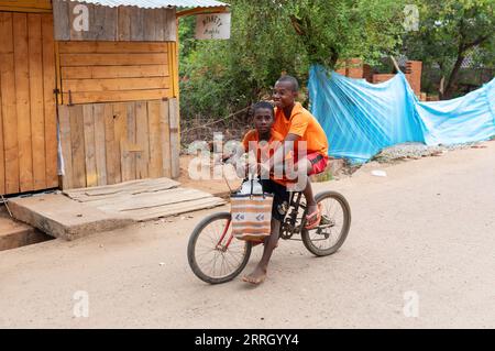 Miandrivazo, Madagaskar - 1. November 2022: Zwei madagassische Jungen fahren mit dem Fahrrad auf einer Landstraße. Eine führt die andere. Stockfoto