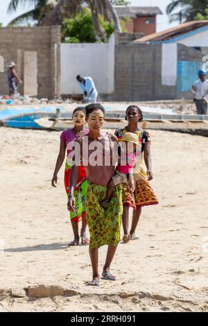 Morondava, Madagaskar - 3. November. 2022: Madagassische Frau mit ihrem Gesicht gegen die Sonne gemalt, mit Kind in den Armen, geht am Hafen von Morondav entlang Stockfoto