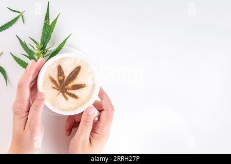 Medizinisches Cannabis Hanf Kaffee Latte. Tasse cremiger geschlagener Kaffee mit Cannabisöltropfen und gezeichnetem Blatt, mit Hanfblättern auf weißem Hintergrund Stockfoto