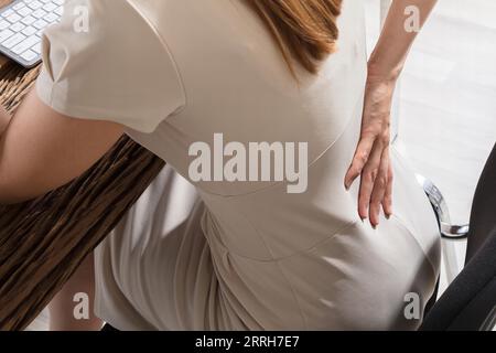 Junge Geschäftsfrau in Rückenschmerzen Sitzen auf Stuhl am Arbeitsplatz Stockfoto