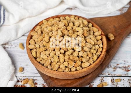 Getrocknete Maulbeeren in einer Holzschale. Sonnengetrocknete Maulbeere auf weißem Holzgrund. Nahaufnahme Stockfoto