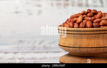 Erdnüsse in Holzschale. Erdnüsse in der Schale auf weißem Holzgrund. Leerzeichen kopieren. Leerzeichen für Text Stockfoto