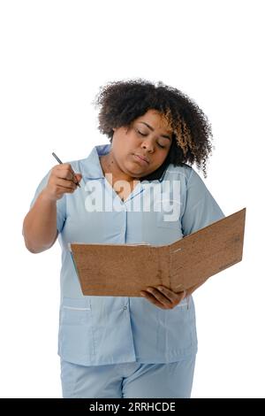 Junge Afro-Latina-Krankenschwester in blauer Uniform, die beim Telefonat steht und sich in der Mappe mit Stift Notizen macht, vertikales Bild auf weißem Hintergrund Stockfoto