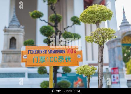 Bangkok, Thailand - 9. Mai 2023: Ein Schild am Eingang zum Wat Suthat kündigt auf Englisch und Chinesisch an, dass Ausländer 100 Baht für die Einreise zahlen müssen Stockfoto