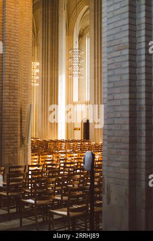 Das Innere der Grundtviger Kirche mit Reihen von Holzstühlen und einem Kronleuchter im Hintergrund Stockfoto