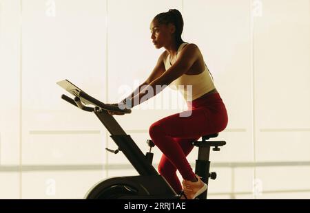 Sportliche schwarze Frau, die sich in ein gesundes Home-Workout-Routine, mit einem Heimtrainer als Teil ihres Fitness-Regimes. Junge Frau, die mit einem trainiert Stockfoto